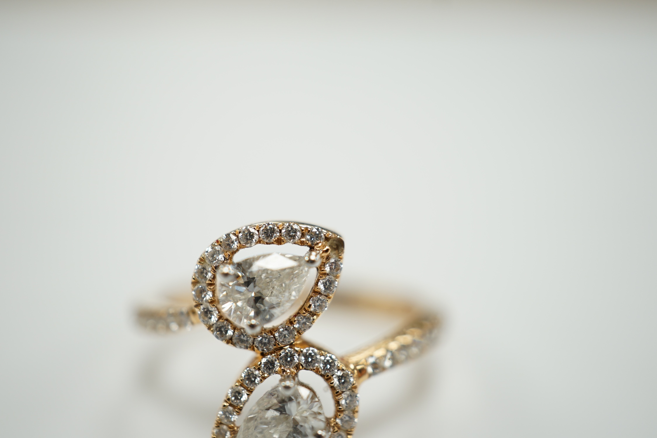 A modern 18k and two stone pear cut diamond set cross-over ring, with diamond chip border and shoulders, size L, gross weight, 2.9 grams.